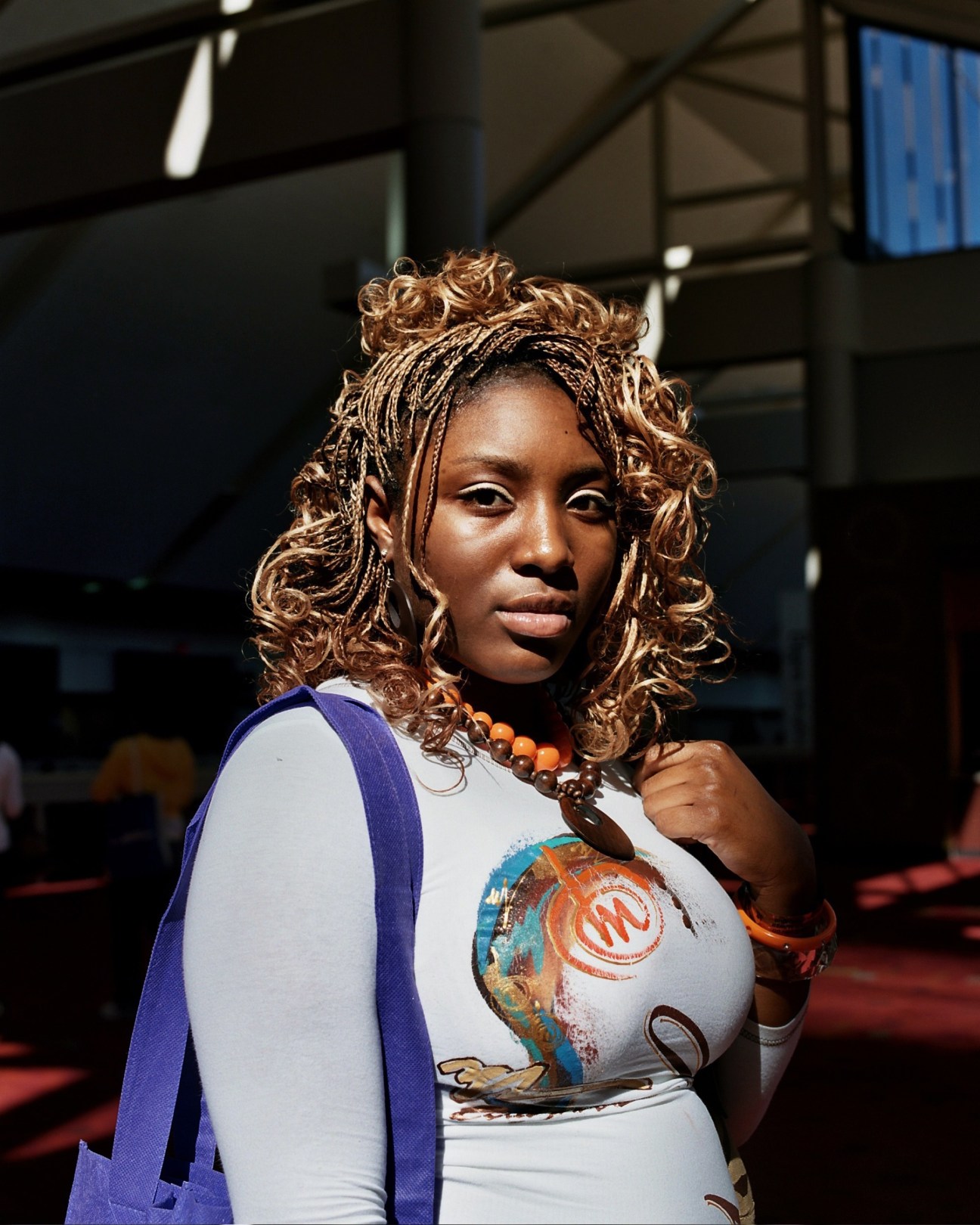 Woman with long curly brown hair extensions wearing a white top and orange beaded necklace at the hair show.