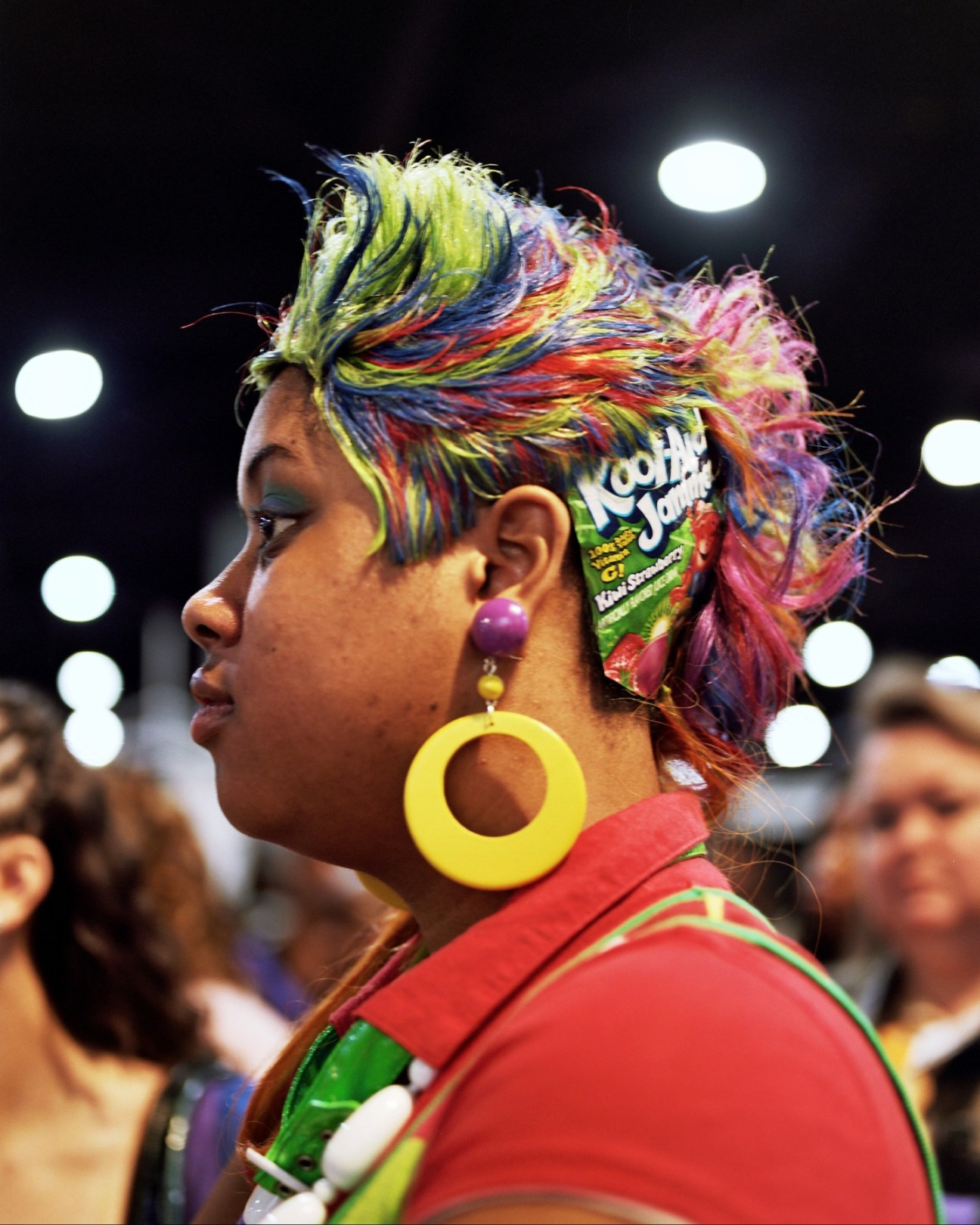 Woman wearing colorful rainbow hair extensions and yellow hoop earrings at the Bronner Brothers hair show.