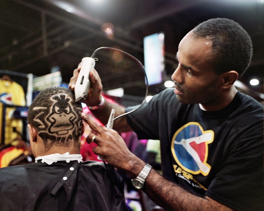 Barber King McLaurin demonstrates razoring technique by creating a detailed Daffy Duck design on a child's head.