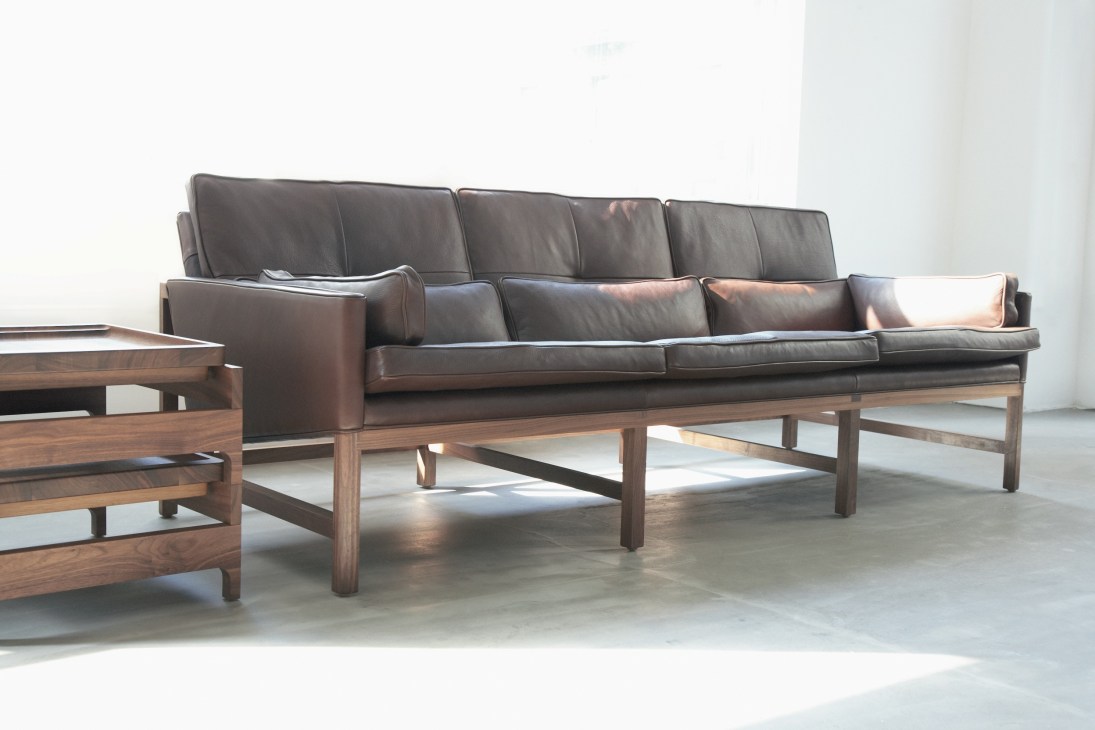 Dark leather sofa with wooden frame and matching wooden coffee table in minimalist interior setting.