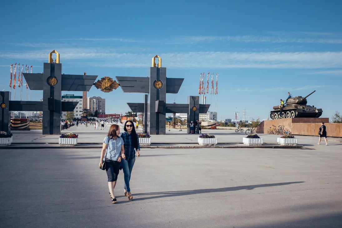 Two women walking in Second World War Memory Alley in Yakutsk with military monuments and flags