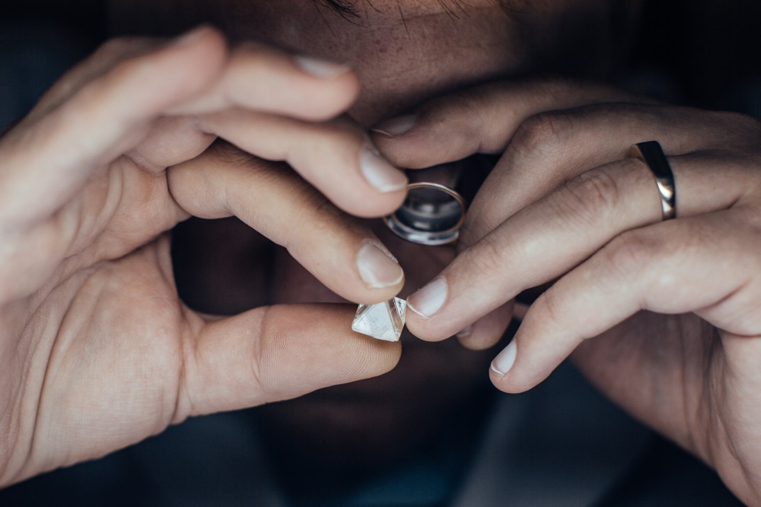 Hands exchanging a diamond stone, with wedding rings visible on their fingers.
