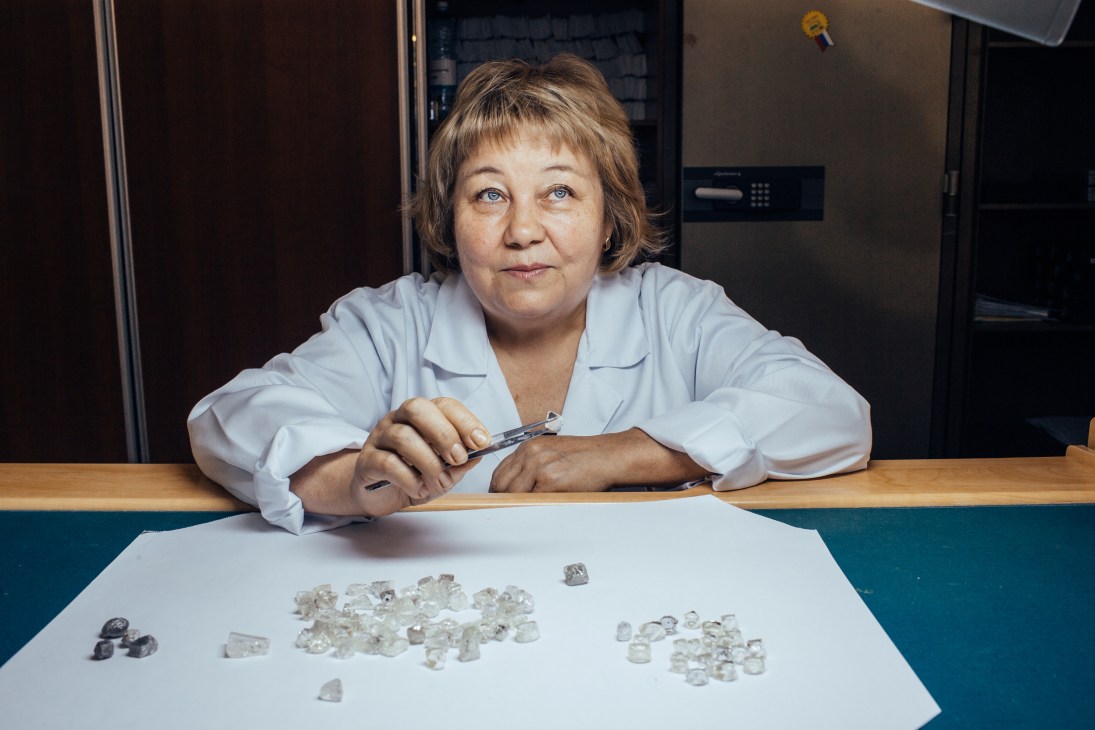 Woman in white lab coat examines sorted diamonds on a table at a sorting facility.