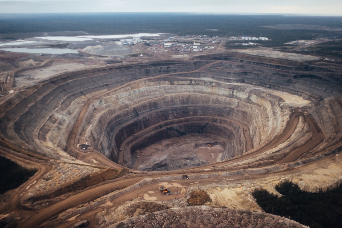 Aerial view of a massive open-pit diamond mine with concentric circular excavation levels and surrounding industrial facilities.