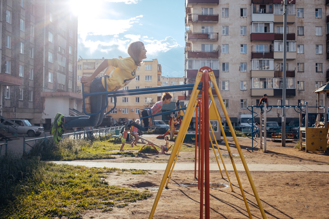 Children playing on colorful playground equipment in a courtyard surrounded by Soviet-era apartment buildings in Mirny.