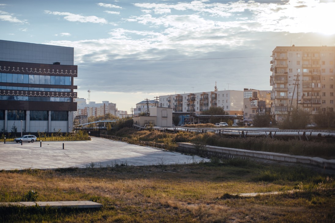 Urban riverside landscape with modern buildings, permafrost stilts, and industrial infrastructure in Yakutsk.