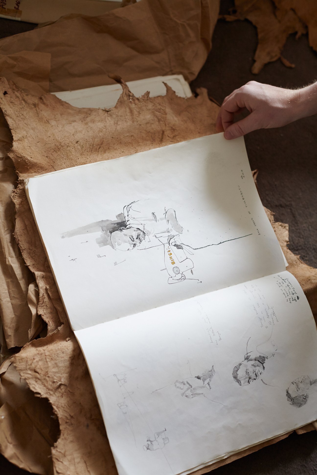 Person holding open a sketchbook with ink and watercolour drawings from George Butler's trip to West Africa.