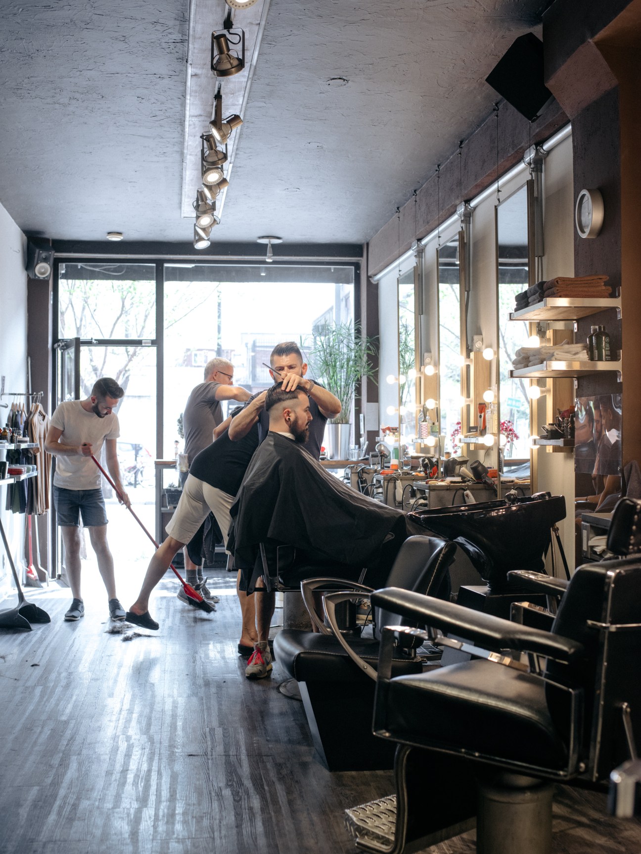 Barber giving a customer a haircut inside Mohawk Barbiers shop with modern interior and large windows.