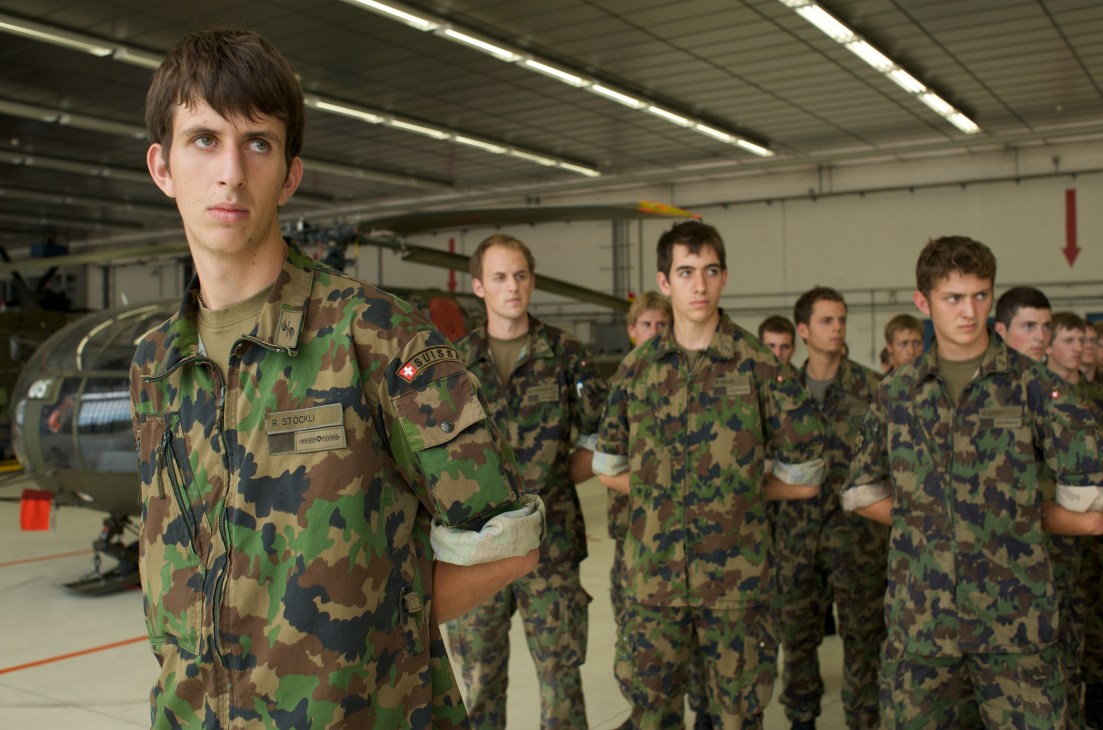 Swiss conscripts in camouflage uniforms stand in formation inside a military hangar at Payerne.