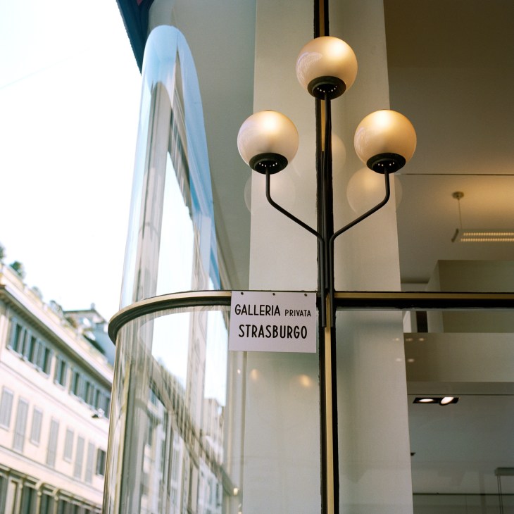 Three frosted glass globe lamps mounted on a black metal pole in Galleria Strasburgo arcade.