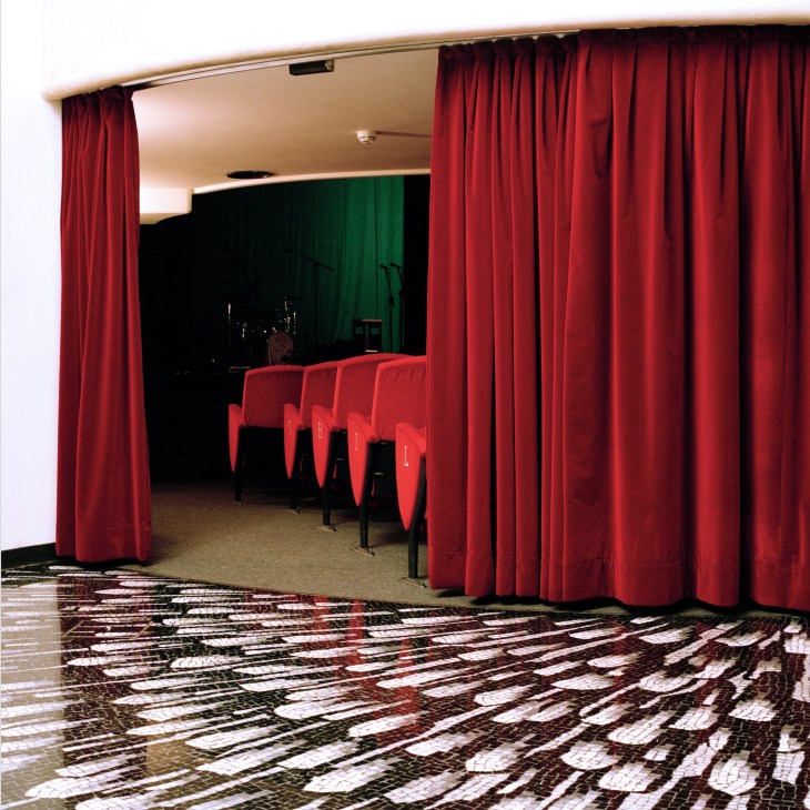 Teatro Filodrammatici theatre foyer with red velvet curtains framing entrance to auditorium with patterned mosaic floor.