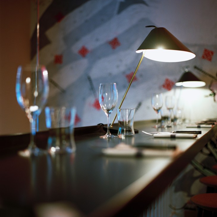 Base Ghisa brass table lamps illuminate a dining table set with glassware at Milan restaurant Pisacco.