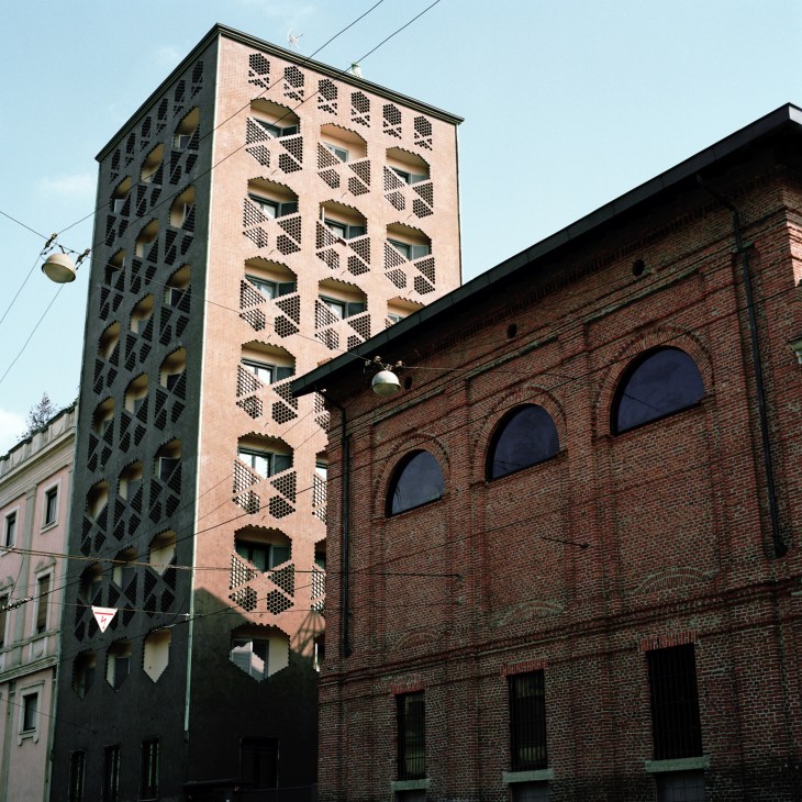 Tall modernist residential tower with hexagonal ceramic tile pattern and recessed windows in shades of pink and dark tones.