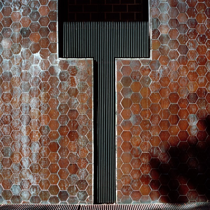 Hexagonal terracotta tiles with a vertical metal door or shutter detail on a building façade.