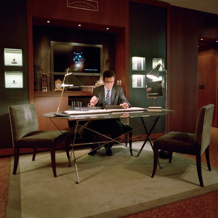 Man in suit works at a glass Cavalletto table with Azucena lamps in a modern watch retailer showroom.