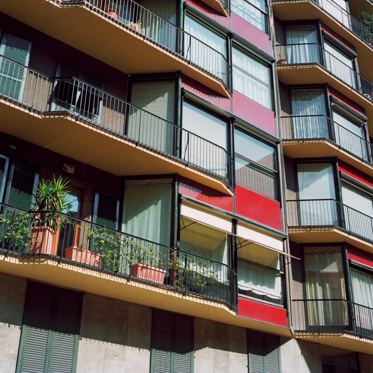 Colorful mid-century apartment building facade with overlapping balcony sliding doors and shutters in red, green and white.