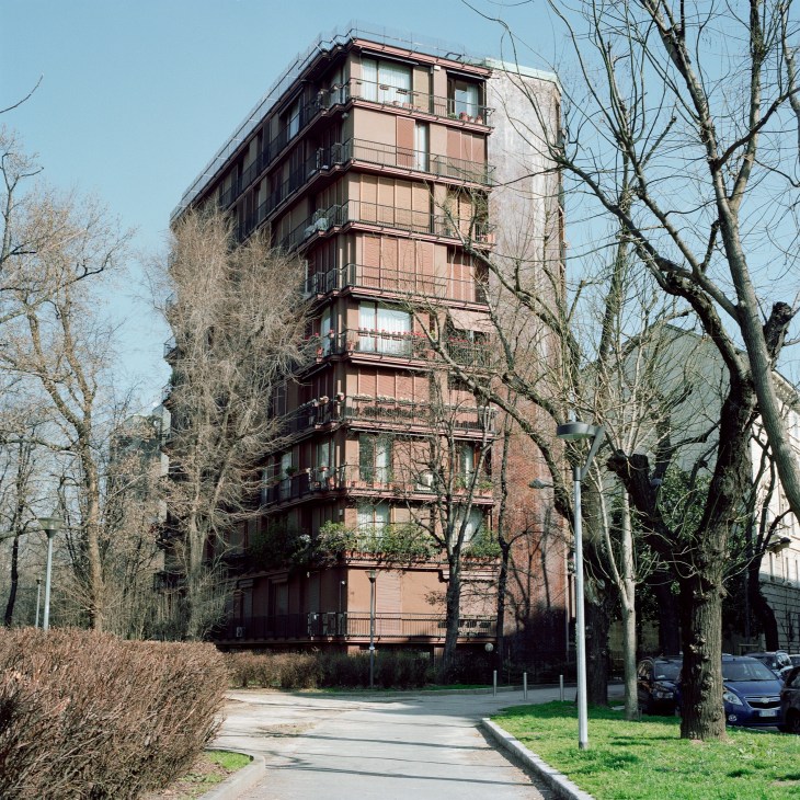 Modernist residential tower with tapered corners, overlapping balcony doors, and hexagonal patterned ceramic tile facade in Milan.