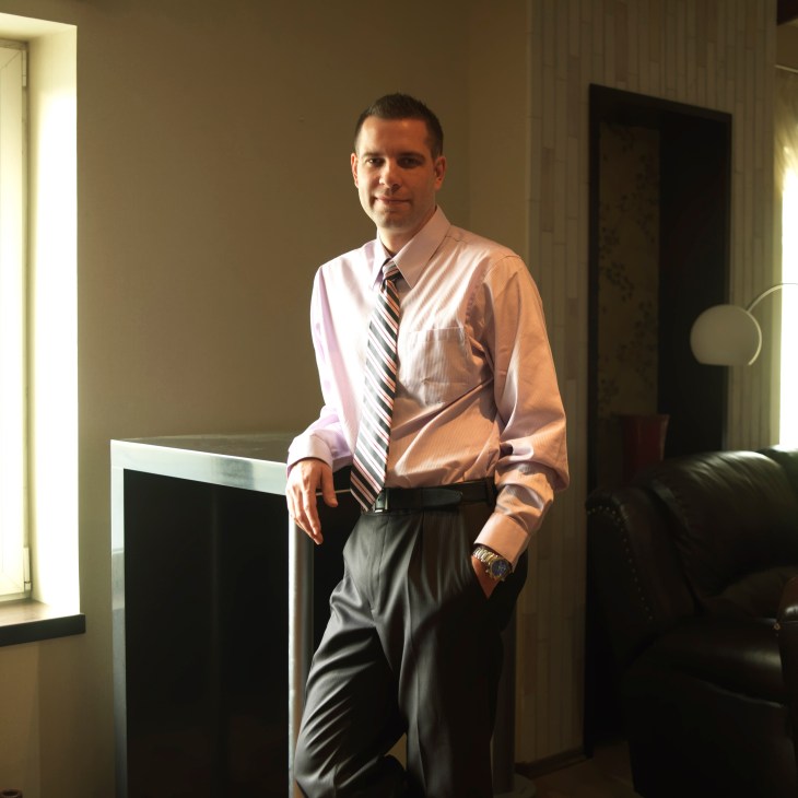 Chris Friend, an American businessman, stands in an office wearing a pink shirt and striped tie.