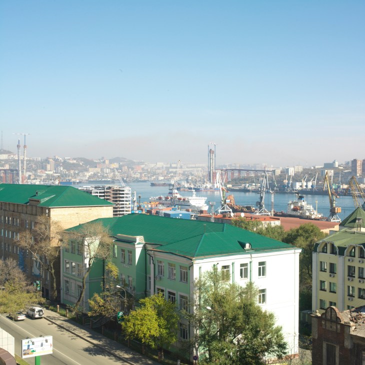 Panoramic view of Vladivostok port with cargo ships, cranes, and residential buildings in foreground