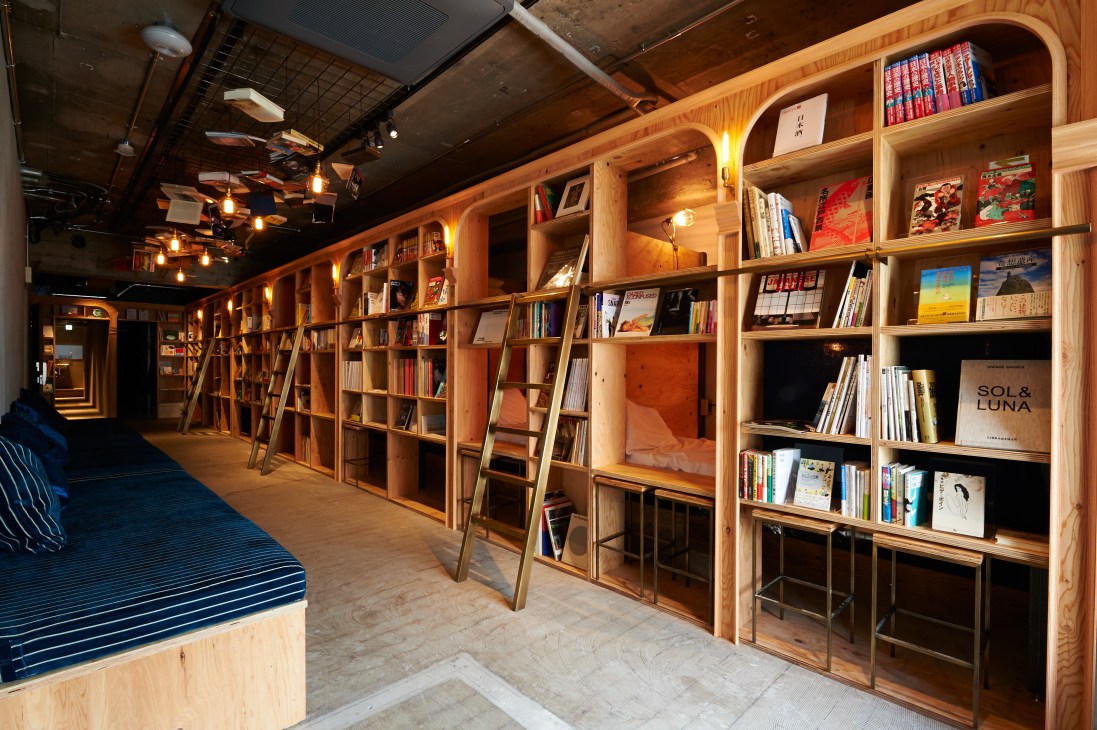 Book and Bed Tokyo hostel interior with wooden bookshelves lining walls and a reading nook with cushions.