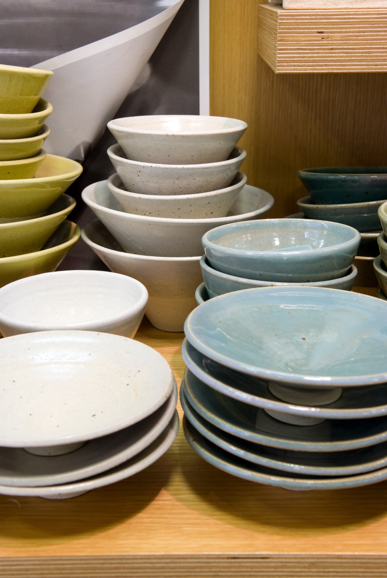 Stacked ceramic bowls and plates in cream, white, and blue glaze displayed on wooden shelves.