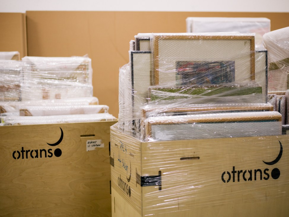Paintings wrapped in plastic and secured with wooden supports inside branded Otrans shipping crates.