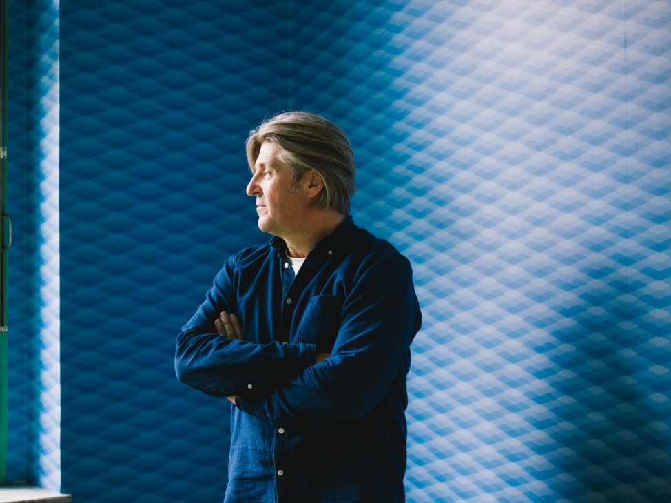 Architect Ludvík Grym stands with crossed arms against a blue tiled wall.