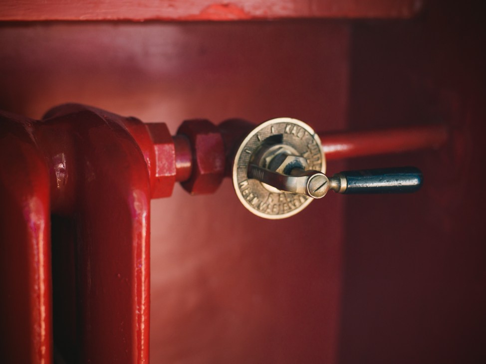 Close-up of an ornate brass valve handle on a red radiator against a red wall.