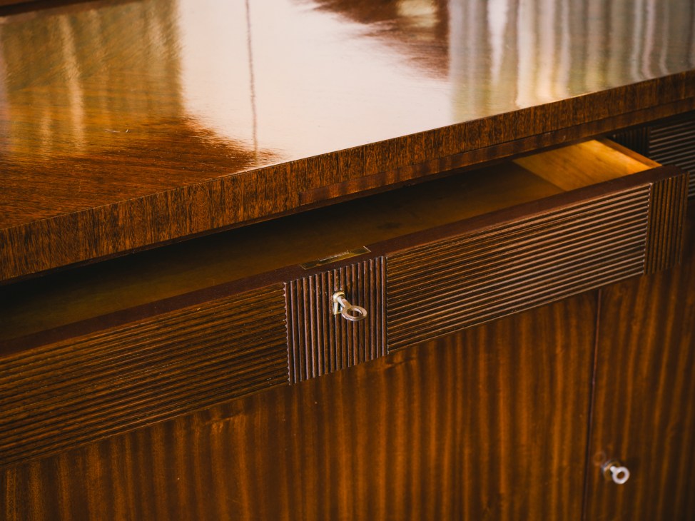 Detail of a wooden sideboard with vertical fluting and metal handles, showing restored wood grain and finish.