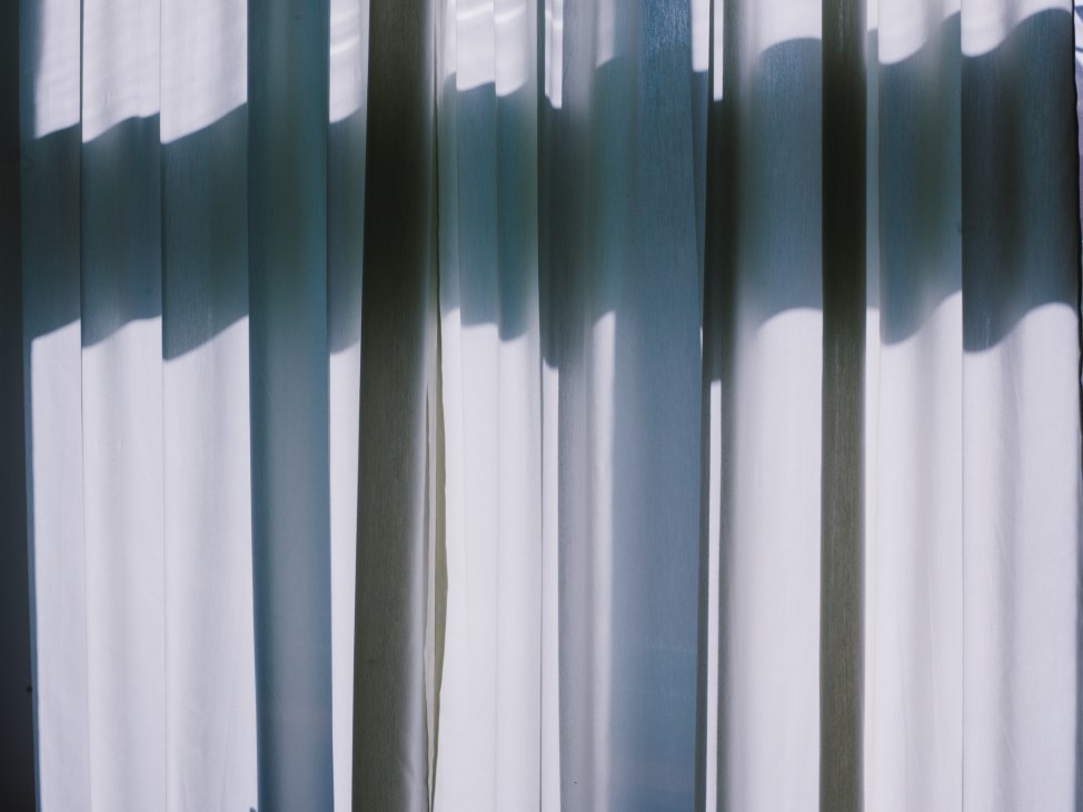 Blue-green and white striped curtain with sunlight casting shadows through vertical pleats.