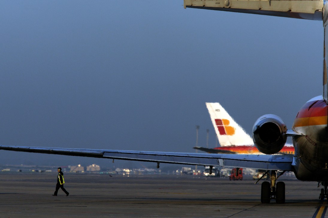 Iberia airline aircraft on tarmac at Barajas airport with ground crew member walking nearby.