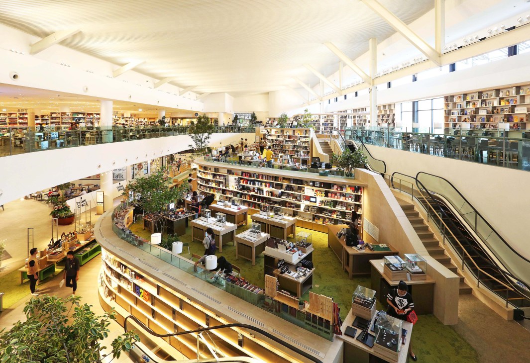 Interior of Think Space B2S bookshop in Bangkok showing two-story space with bookshelves, green flooring, natural light, and scattered visitors.
