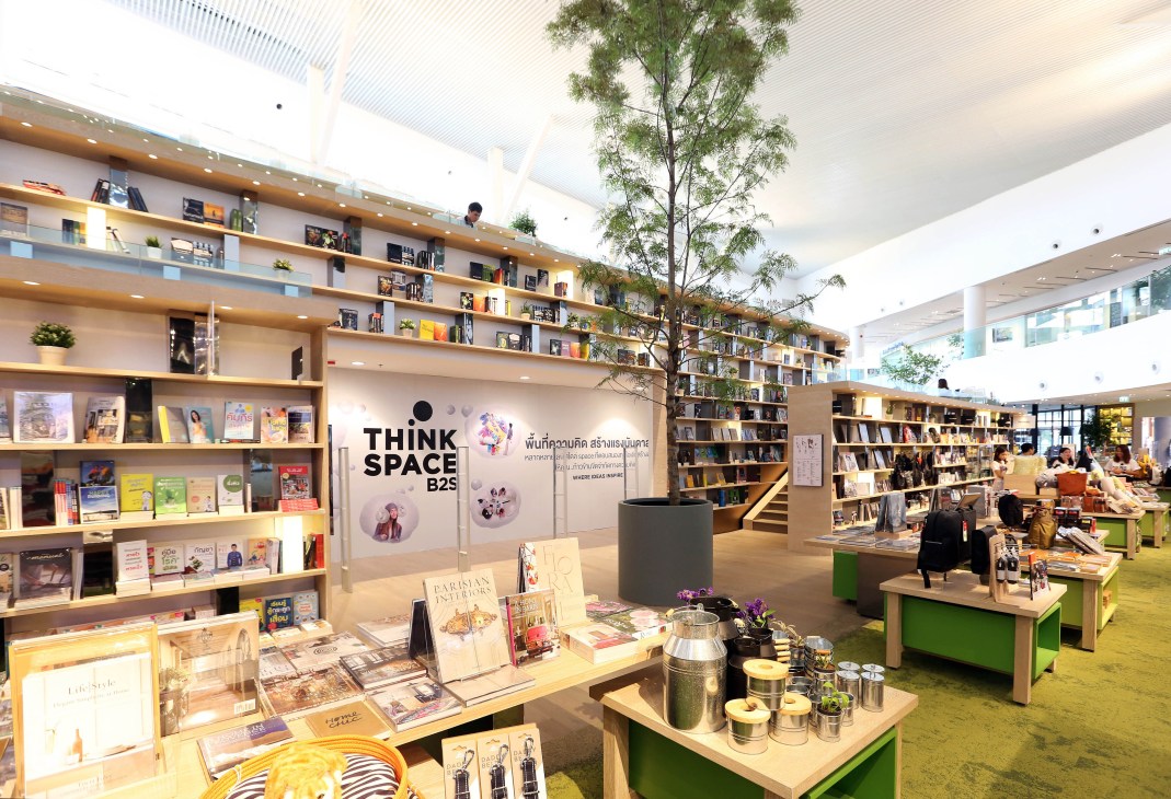 Interior of Think Space B2S bookshop in Bangkok with wooden shelves, books, a tall tree, and green seating areas.