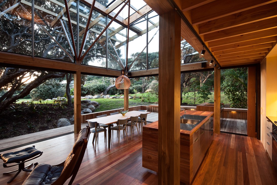 Wood-lined open-plan living and kitchen space with sliding glass doors opening onto a forested landscape.
