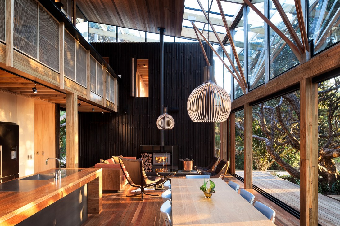 Open-plan living and dining area with wood elements, hanging pendant lights, fireplace, and large glass doors opening to forest views.