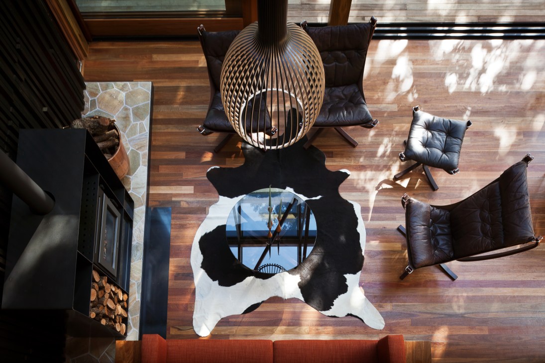 Overhead view of living area with woven pendant light, black leather chairs, and cowhide rug on wooden floors.