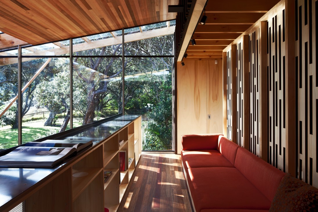 Interior of Butler Beach House mezzanine with red sofa, wooden counter, large windows overlooking trees, and wood-slat ceiling.