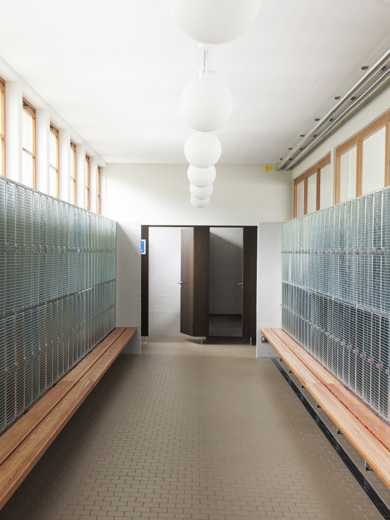 Symmetrical changing room corridor with metal-mesh lockers and wooden benches at Strandbad Wollishofen.