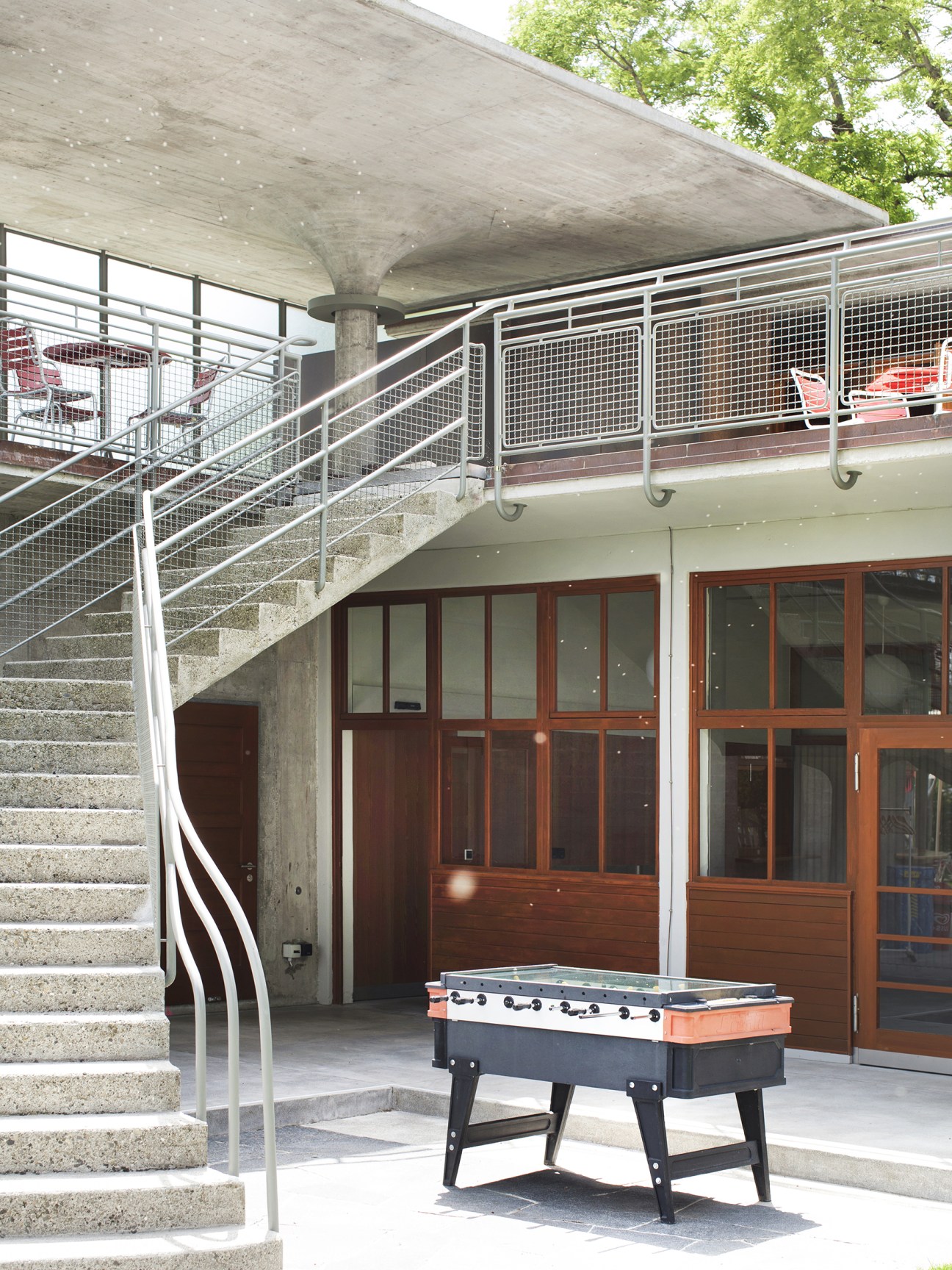 Two-level Strandbad Wollishofen building with concrete stairs, metal railings, wooden doors, and a foosball table on the lower level.