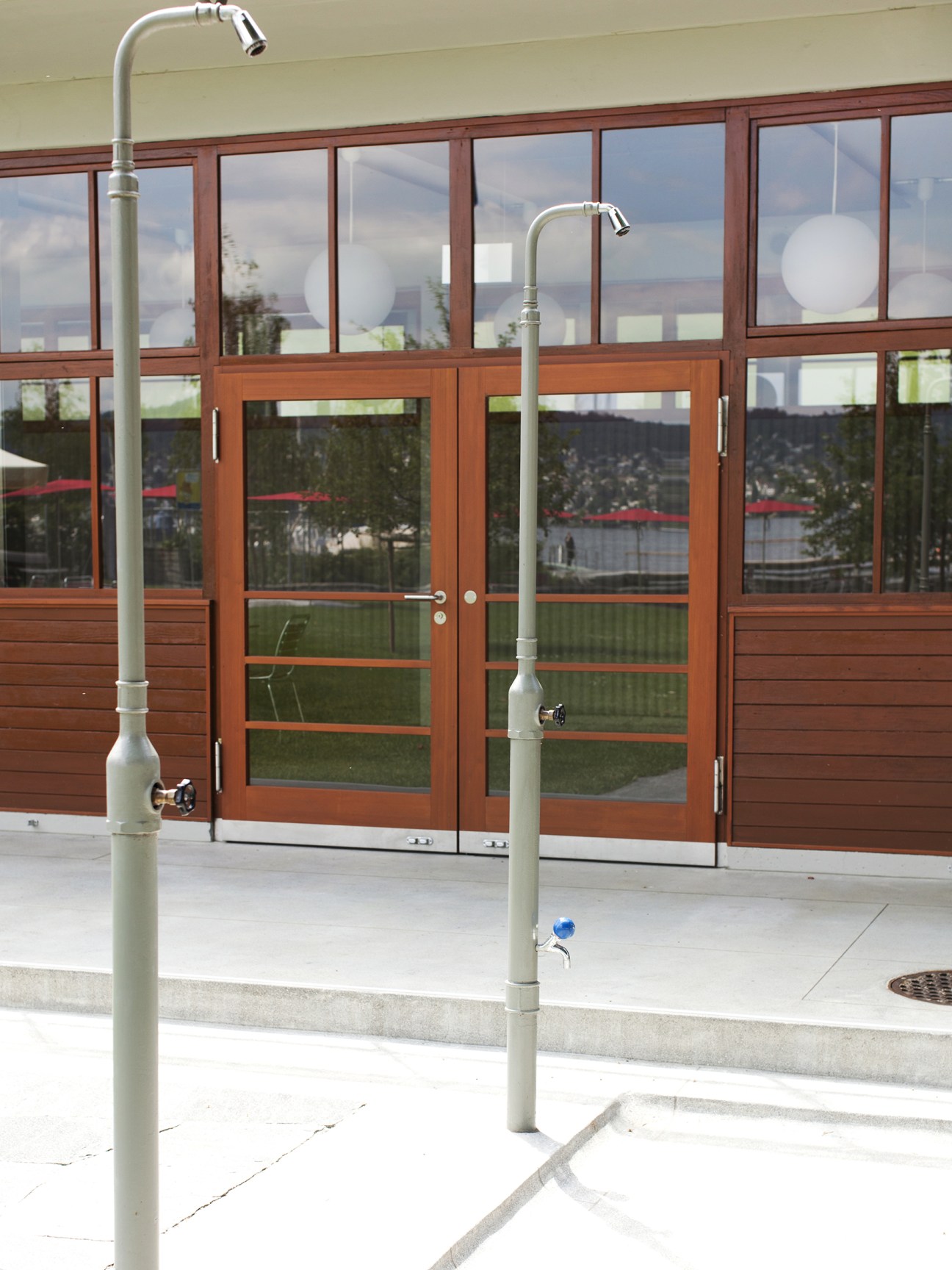 Outdoor shower fixtures on concrete patio with restored wooden building and lake view.