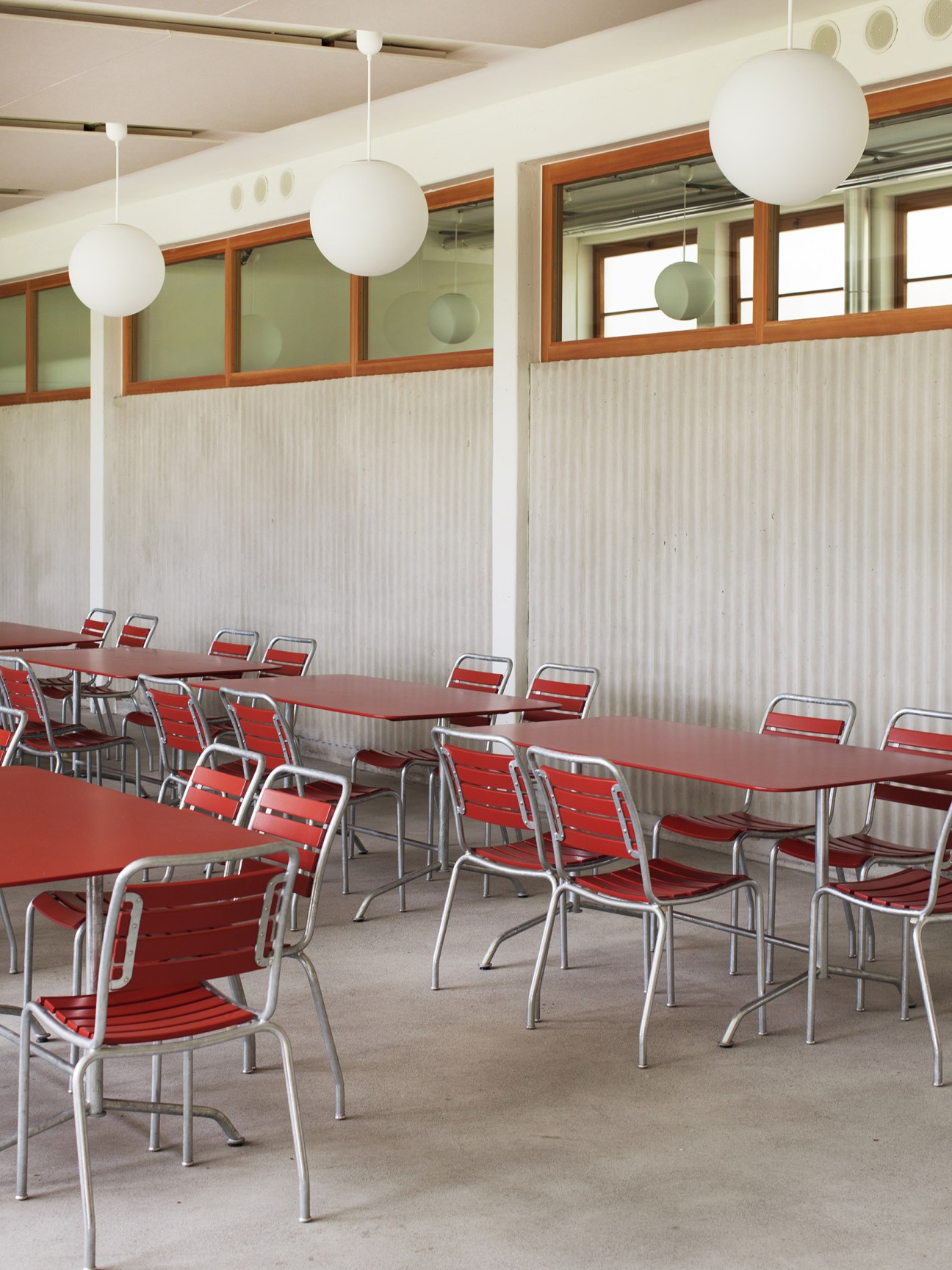 Dining area with red chairs and tables in a bright modern interior with wood-framed windows and pendant lights.