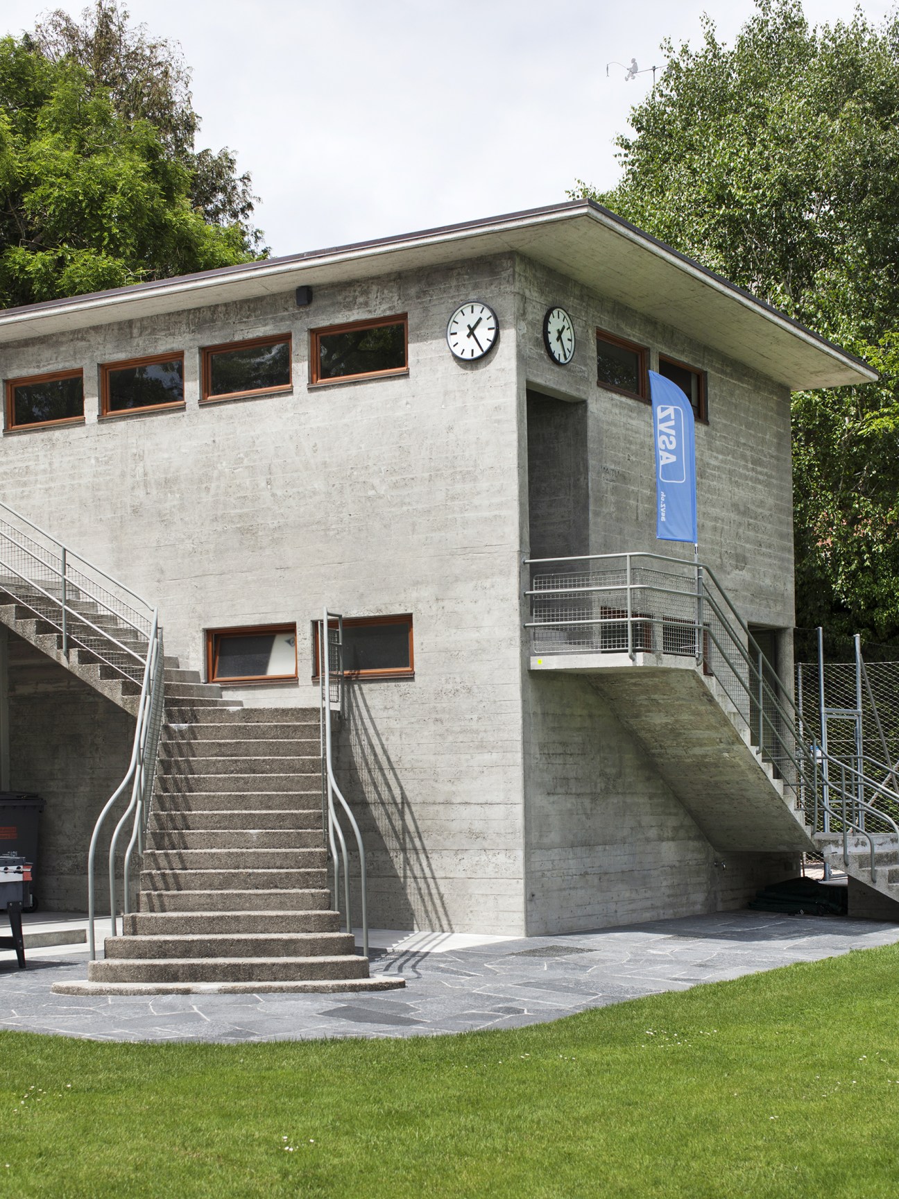 Concrete Strandbad Wollishofen building with two clocks on facade and metal stairs.