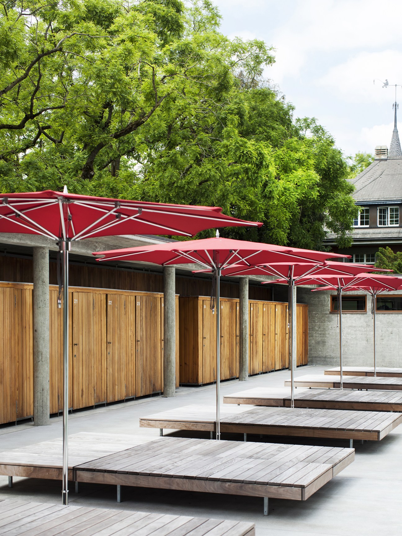 Lounge areas at Strandbad Wollishofen with red umbrellas and wooden deck platforms.