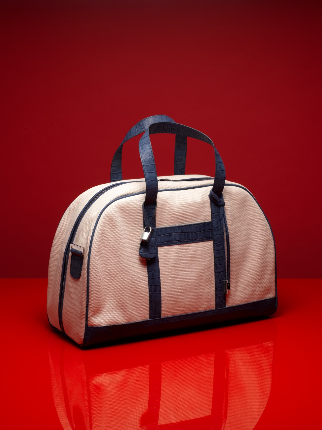 Sartie luxury bag with cream canvas and dark blue leather handles and trim against red background.