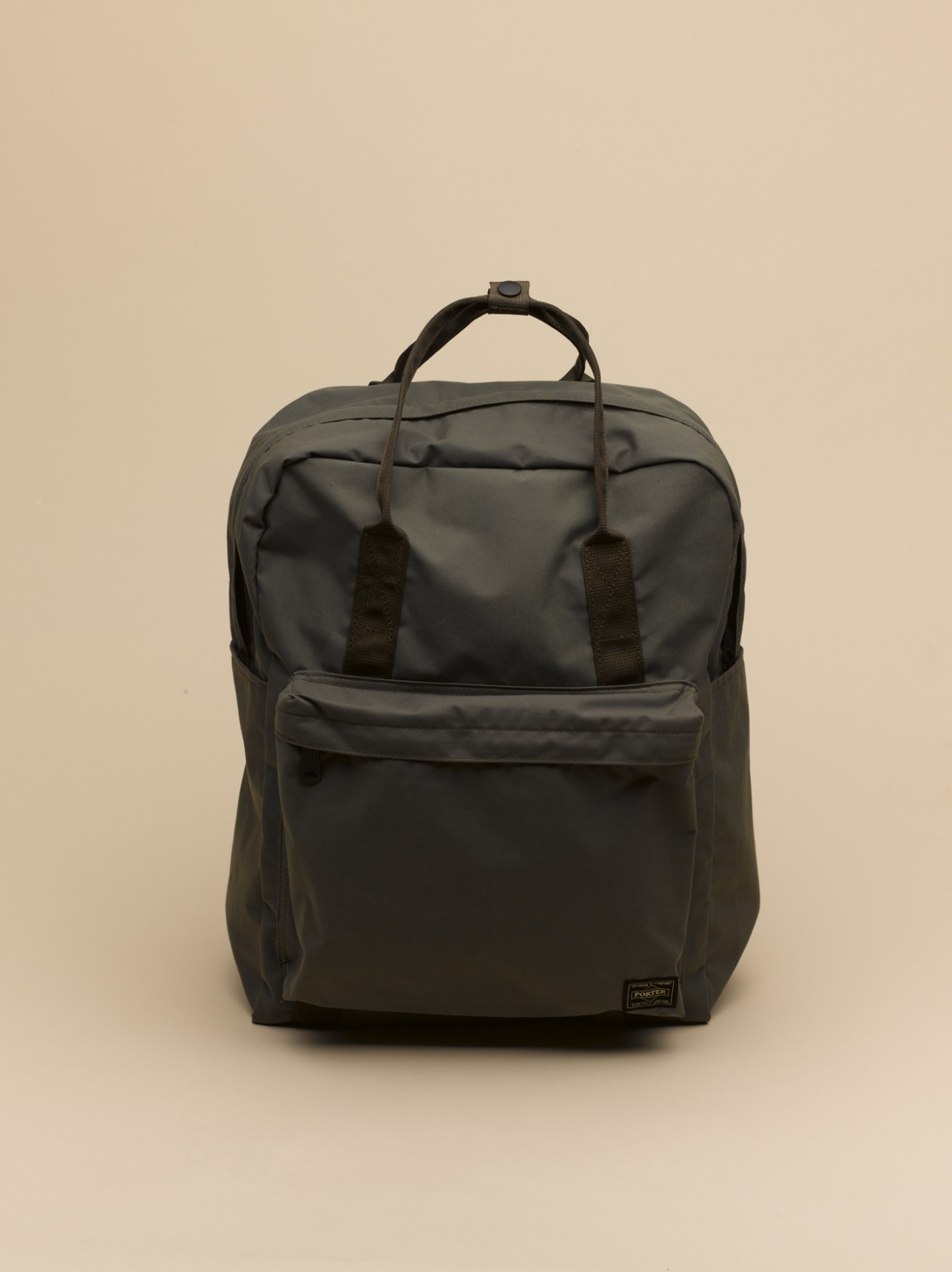Porter black backpack with dual handles and front pocket against beige background.