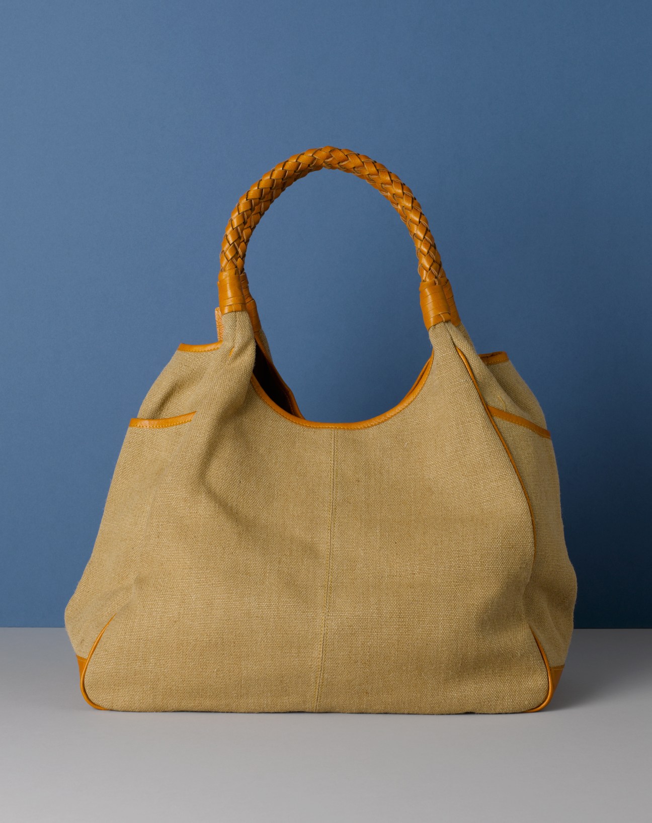 Motherhouse beige canvas handbag with braided orange leather handles against blue background.