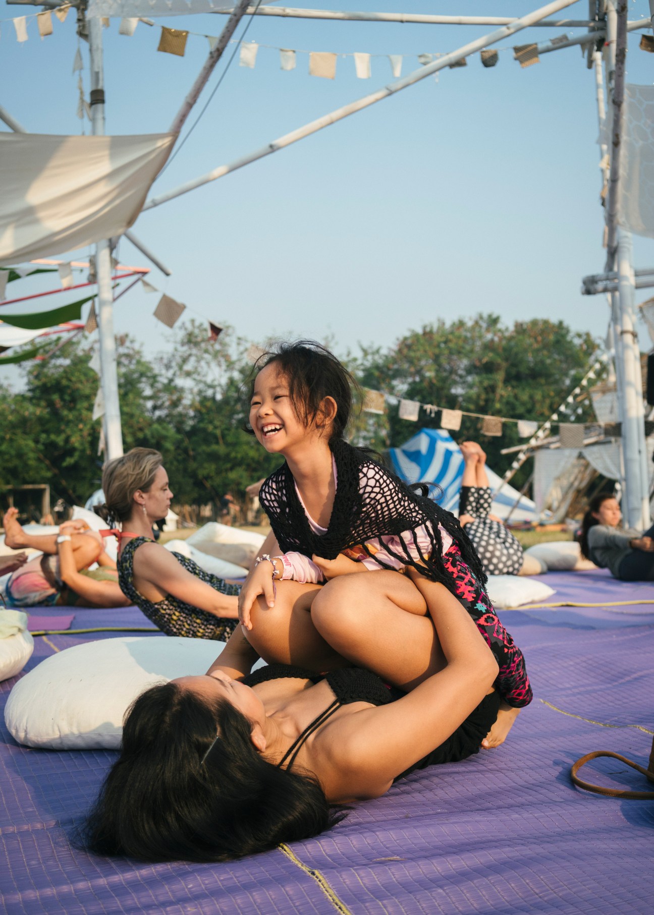 Festival attendees practicing yoga on a purple mat under a white canopy structure at Wonderfruit festival.
