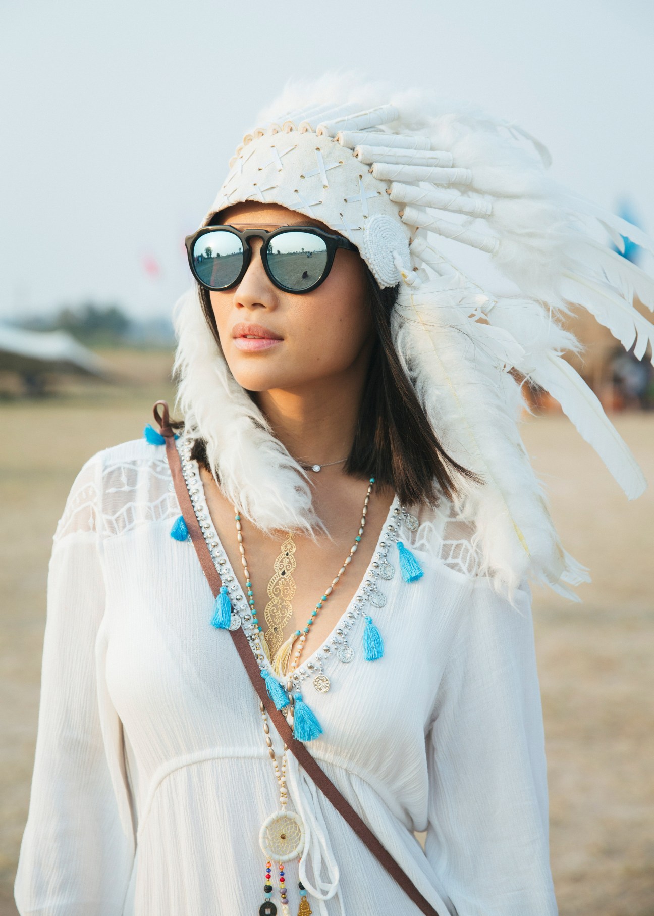 Festival attendee wearing white feathered headdress, mirrored sunglasses and boho accessories at Wonderfruit.