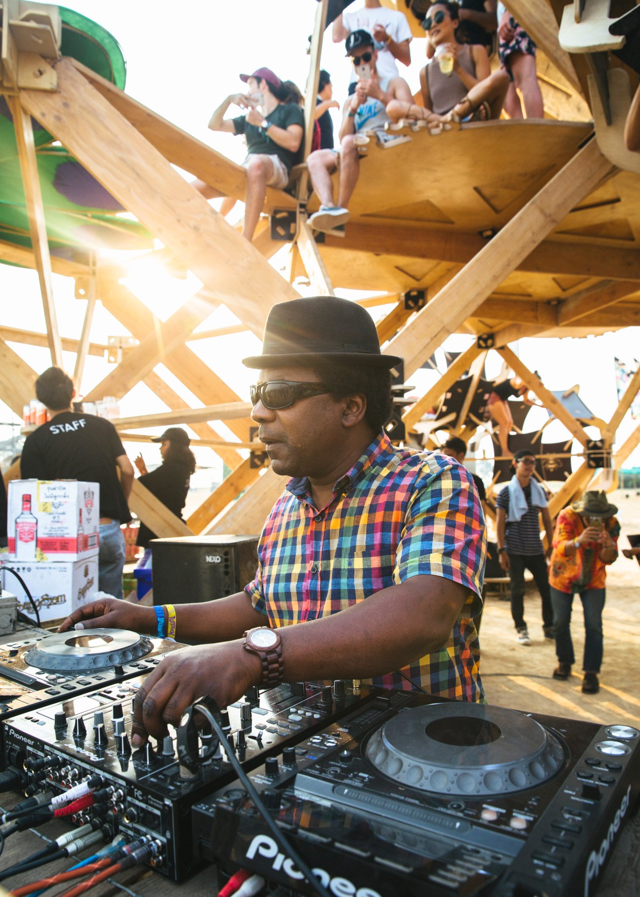 DJ Norman Jay performing at turntables under a wooden stage structure at Wonderfruit festival