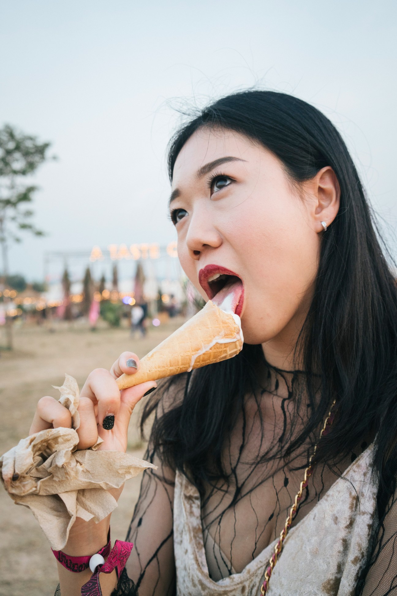 Woman eating an ice cream cone at Wonderfruit festival in Thailand with festival grounds blurred in background.